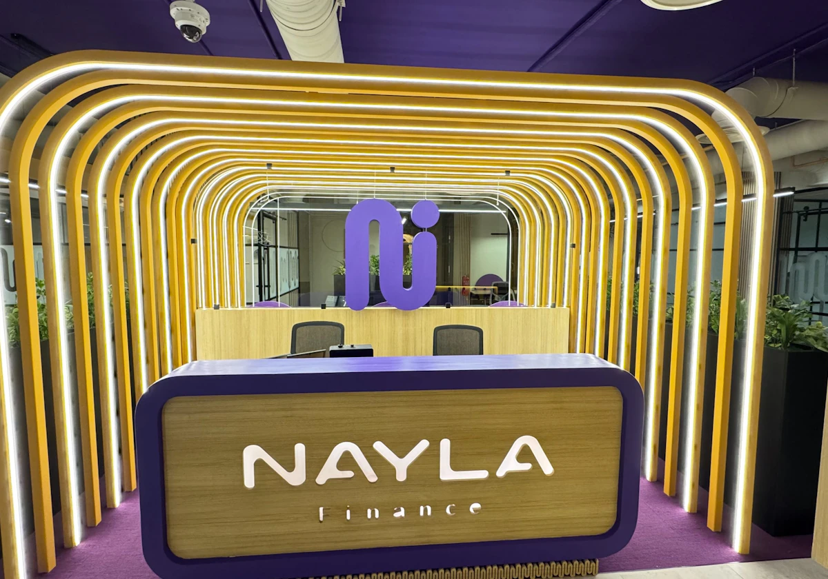 The image showcases a modern office reception area for a company named Nayla Finance, featuring a sleek design with curved golden light fixtures, a purple and wood-accented desk, and green plants enhancing the corporate decor.