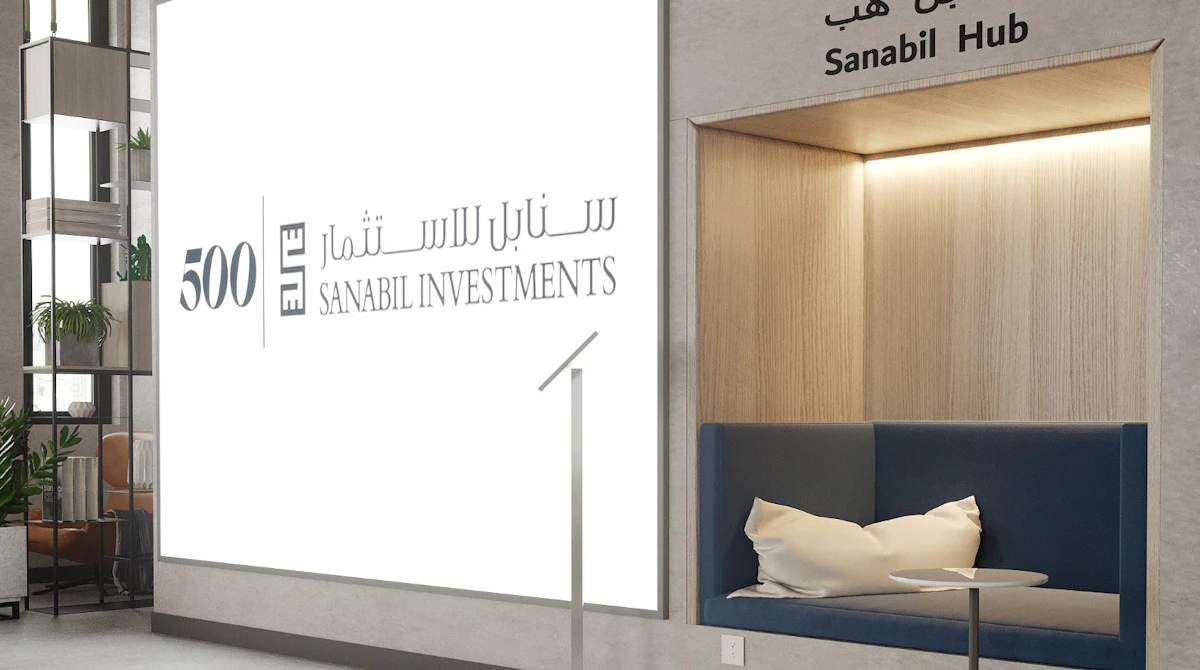 A modern office lobby featuring a large, illuminated Sanabil Investments sign on the wall near a cushioned seating nook, accentuated by a colorful logo and a table, creating a welcoming atmosphere.
