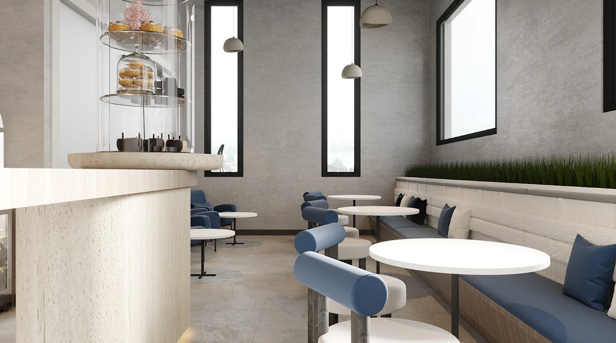 A modern, minimalist café interior featuring a sleek white and blue color scheme, with round tables, cushioned seating against the walls, and a tall central display tower showcasing assorted pastries, accented by large windows allowing natural light to flood the space.
