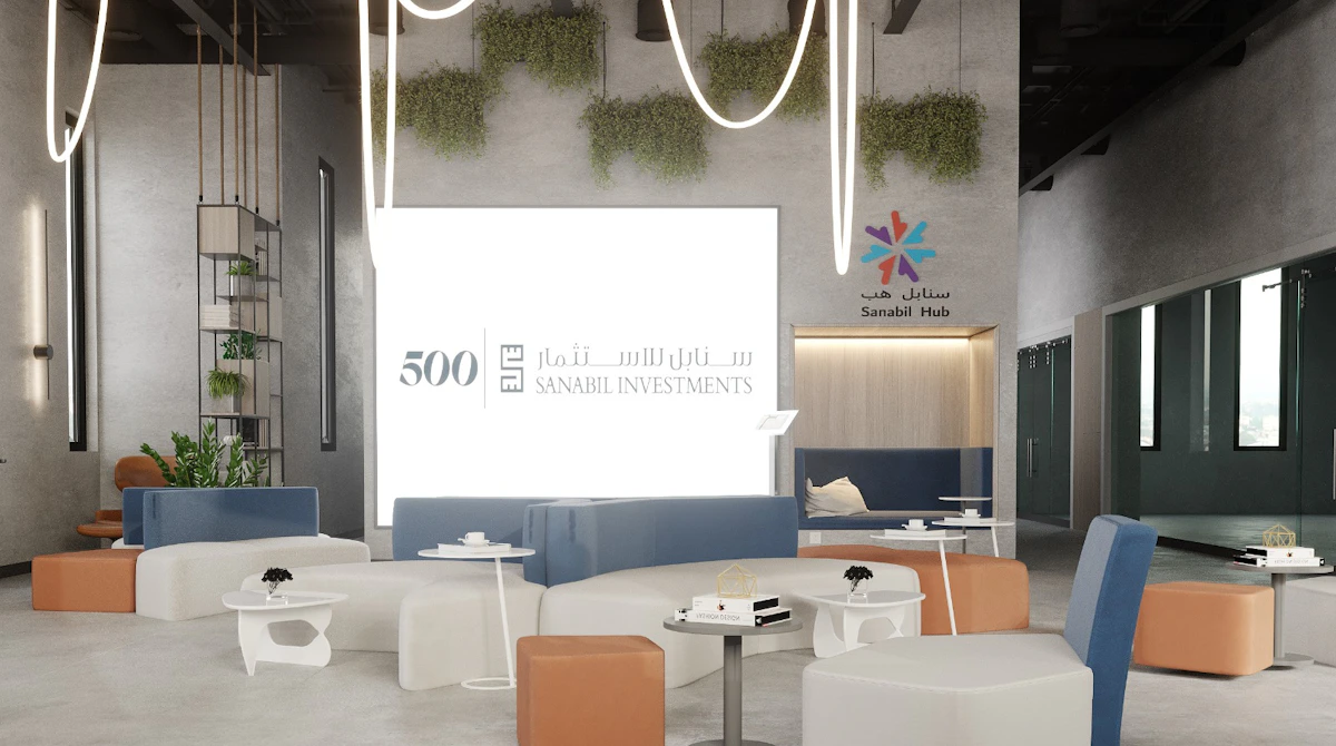 Modern coworking space with contemporary furniture, featuring white tables and chairs, brown and blue seating, hanging lights, green wall plants, and prominent branding for Sanabil Investments and 500 Global.