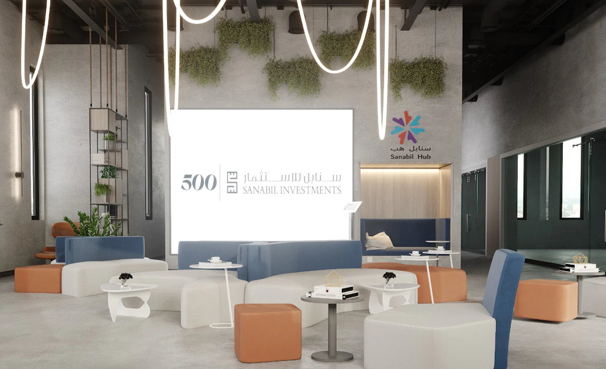 Modern coworking space with contemporary furniture, featuring white tables and chairs, brown and blue seating, hanging lights, green wall plants, and prominent branding for Sanabil Investments and 500 Global.