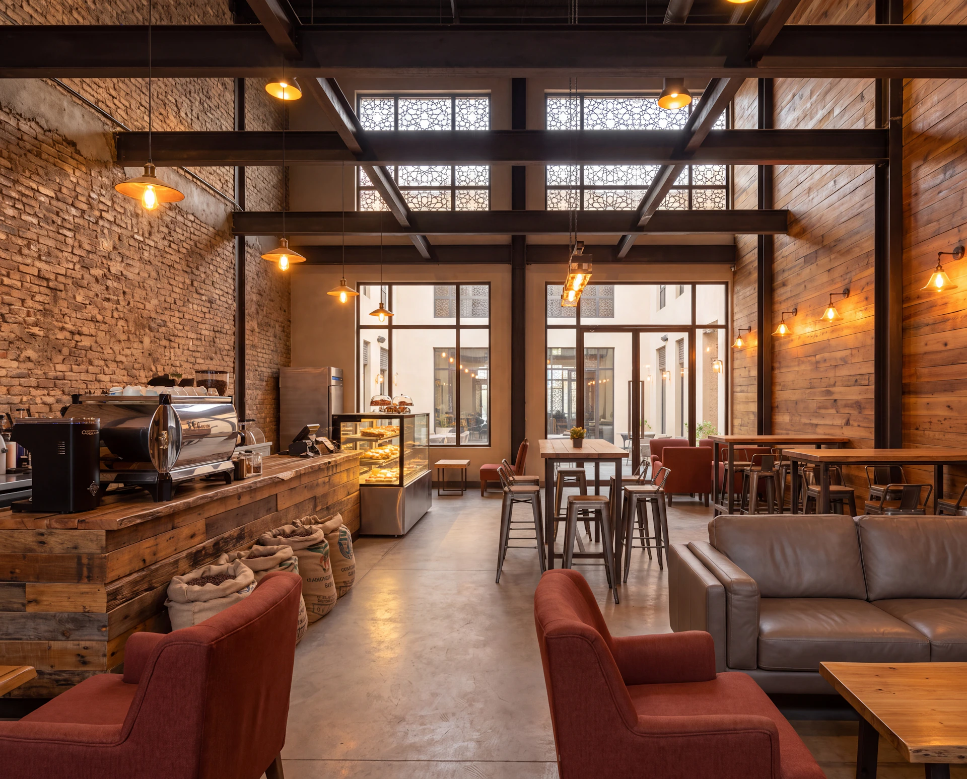Industrial-style café with exposed brick walls and steel beams, glass windows, red and brown leather chairs, wooden counters and tables, stools, and a lit display fridge with food items