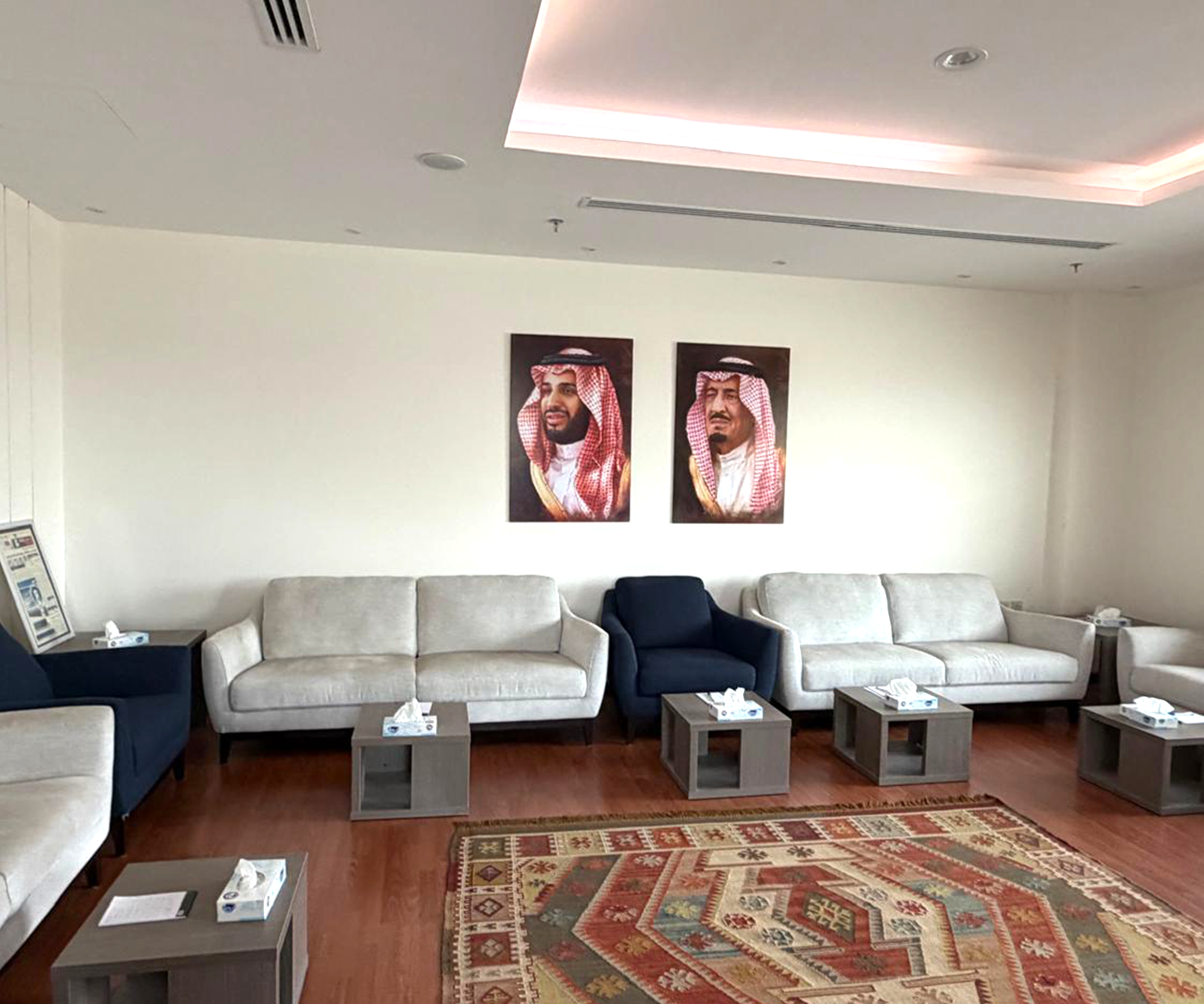 Spacious waiting room featuring cream and navy blue sofas, modern side tables with tissue boxes, a traditional patterned rug, and two portraits on the wall.