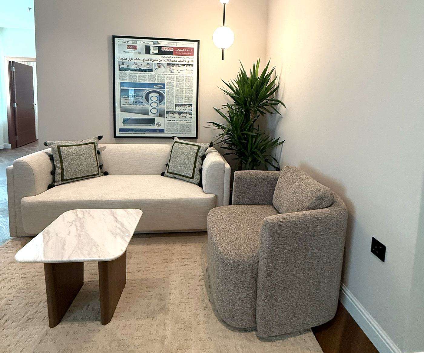 Cozy living room featuring a modern gray loveseat and matching armchair, centered around a sleek marble-top coffee table, with a leafy green plant and framed wall art in the background enhancing the elegant decor.