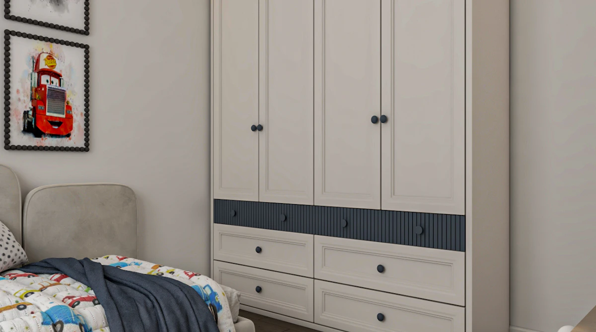 A cozy children's bedroom features a large white wardrobe with blue accents, colorful framed car-themed artwork on the wall, a soft beige headboard, and a playful quilt adorned with cartoon characters, complemented by a plush gray elephant toy on a patterned rug.